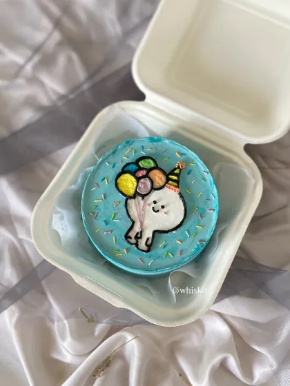 A cute and celebratory bento cake with a hand-drawn character holding balloons. The colorful sprinkles add a festive touch, making it perfect for a small, happy occasion.
