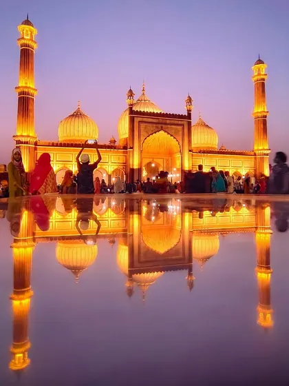 The magnificent Jama Masjid illuminated at dusk, its perfect reflection creating a stunning, symmetrical image of faith and architecture.