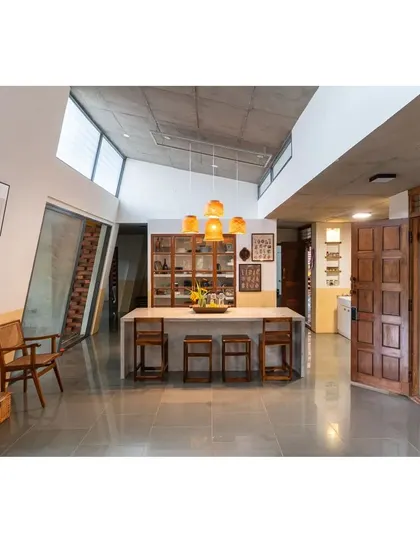 The heart of the 'Aamra' farmhouse, where the dining area flows into the living space. The custom concrete island, wooden bar stools, and upcycled pantry cabinet are all designed to foster connection, blurring the lines between cooking, eating, and living.