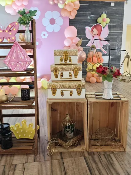 A collection of rustic and chic props, including a wooden ladder shelf, decorative suitcases, and geometric lanterns, used to style a fairy-themed party.