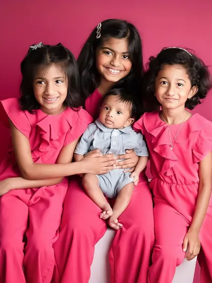 A beautiful portrait of four siblings, with the older sisters lovingly holding their new baby brother. This studio shot captures a precious family milestone.
