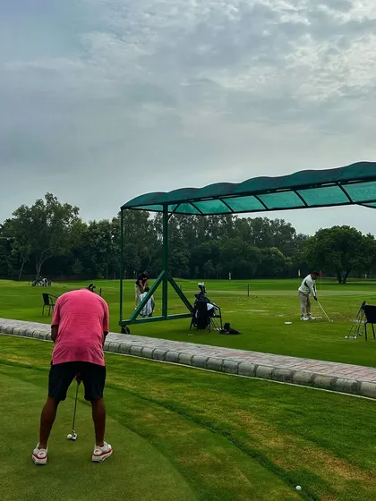 A golfer practices their putting on our undulating green, a key area for lowering scores. The range is visible in the background under a cloudy sky.