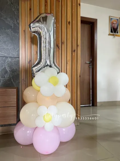A standalone balloon bouquet for a first birthday, featuring a large silver '1' foil balloon on a base of pastel pink, yellow, and cream balloons with small daisy accents.