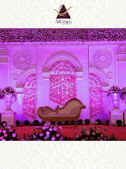A grand reception stage with intricate white and pink architectural details. The design uses dramatic purple lighting and a classic chaise lounge to create a royal and opulent atmosphere.