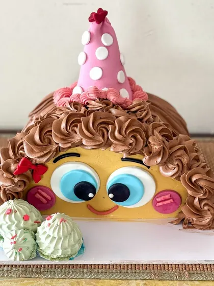Celebrating one and a half years with this adorable half-cake. It's designed to look like a cute character with big eyes, a party hat, and curly chocolate buttercream hair.