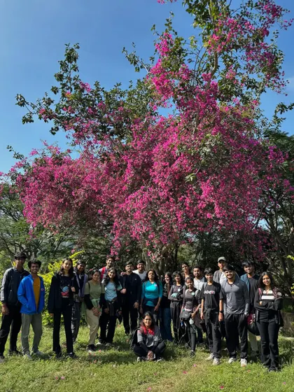 A large group of students from AMC Engineering College standing in front of a beautiful bougainvillea tree. Our treks combine natural beauty with valuable learning experiences.