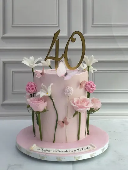 A sophisticated cake for a 40th birthday. The soft pink tier is decorated with delicate, individually placed sugar flowers and butterflies, creating the look of a whimsical garden growing up the side of the cake.