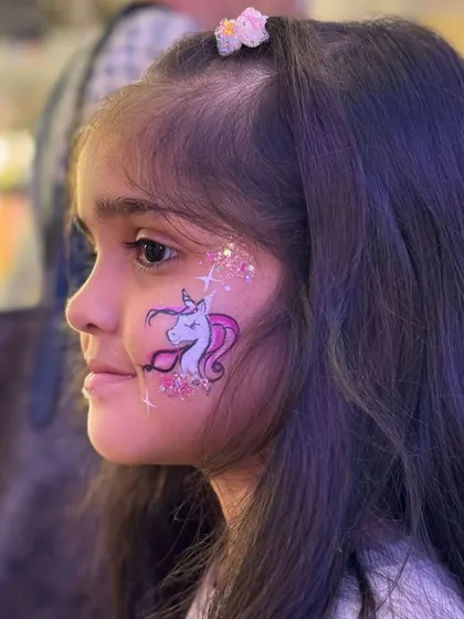 A close-up of a perfectly painted unicorn on a smiling child. The glitter adds that extra touch of magic.