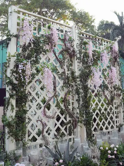 A white lattice wall covered in climbing vines and pink flowers serves as a beautiful and textured backdrop, perfect for photos or to define a specific area of the event.