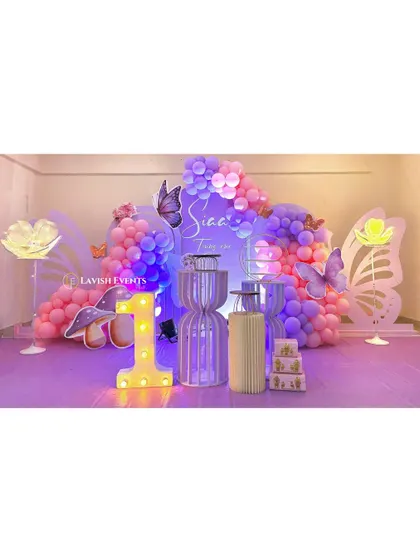 An enchanting butterfly-themed party with purple and pink lighting, large glowing butterfly wing props, and a light-up number '1' for a magical first birthday.