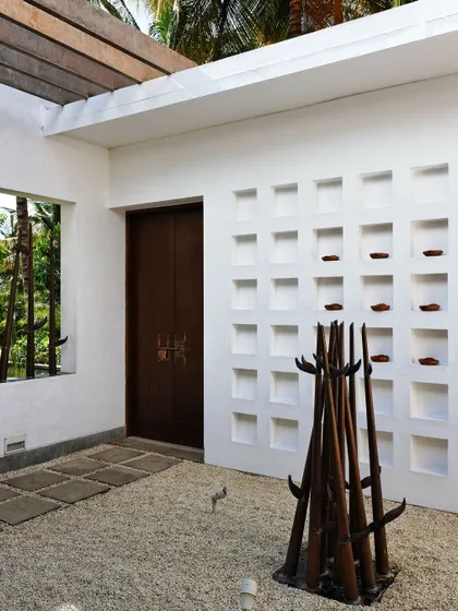 The entrance to 'The Tropical House' features a simple gravel courtyard with a sculptural art piece and a wall of niches, creating a tranquil threshold between the outside world and the home within.