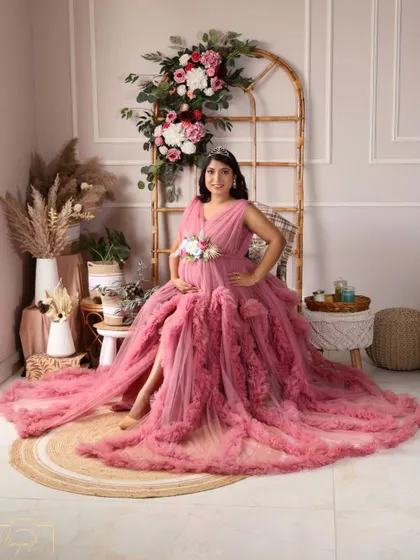 A stunning full-length portrait in a pink ruffled gown, showcasing the beauty of the dress and the radiant mama-to-be in the boho setup.