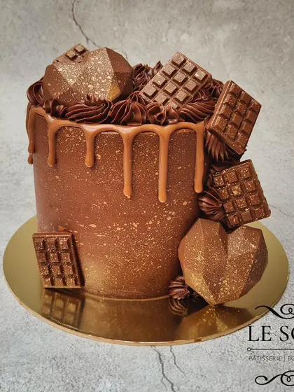 Look at that shine. This 1 kg Chocolate Truffle cake is pure indulgence, decorated with geometric chocolate hearts, mini chocolate bars, and a caramel drip.