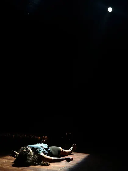 An actor lies on the stage under a single spotlight during a tech run for "Gretel."