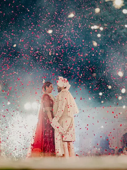 A shower of rose petals rains down on the couple. This magical moment, set against a backdrop of fireworks, is a perfect blend of grandeur and romance.