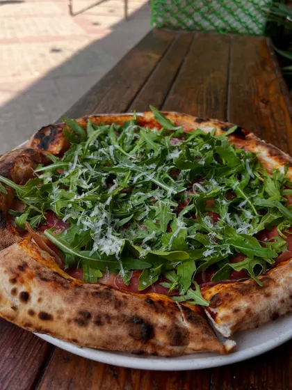 The full view of our Prosciutto di Parma e Rucola pizza on a rustic wooden table.