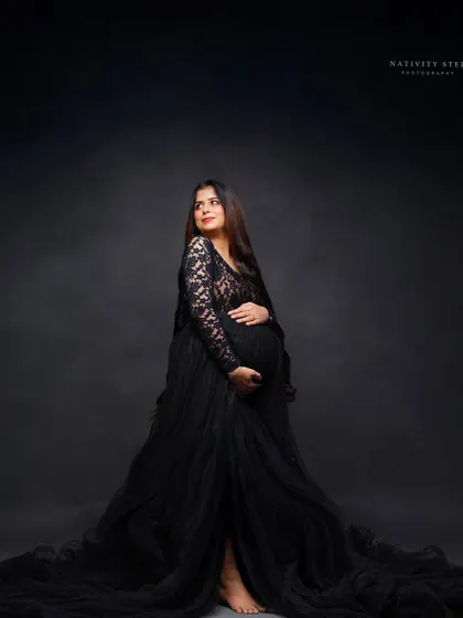 A full-length portrait in a dramatic black lace and tulle gown. This shot highlights the elegant silhouette of the mother-to-be against a classic dark backdrop.