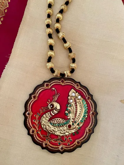 A detailed shot of the red peacock Tanjore pendant, focusing on the delicate stonework and the texture of the gold foil.