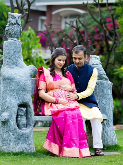 A tender moment where the father-to-be cradles the baby bump. This outdoor shot in a traditional saree captures the anticipation and love.