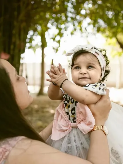 A mother holds her baby girl up high during an outdoor shoot. The sunlight filtering through the trees adds a magical quality to this loving moment.
