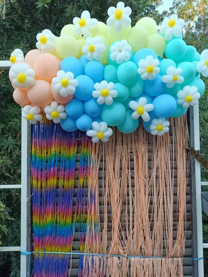 We combine different elements to create unique backdrops, like this butterfly and floral-themed setup for a fourth birthday. It features a colorful balloon cloud adorned with daisy accents and a textured fringe curtain for a truly magical photo spot.
