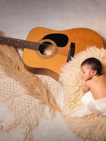 A future musician dreaming of his first song. This setup with a guitar and warm candlelight creates a cozy and artistic atmosphere for a newborn shoot.