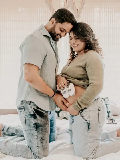 A relaxed and happy at-home maternity photo. This candid moment on the bed, with the couple holding tiny baby shoes on the bump, feels so natural and full of love.