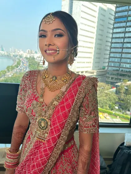 A beautiful bride with a stunning view of Mumbai behind her. Her hair is styled in a classic updo to match her traditional red and gold outfit.