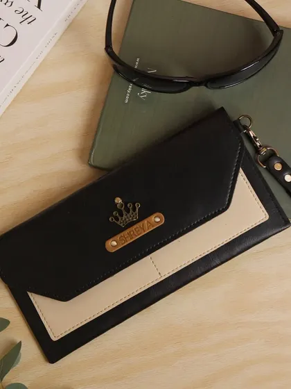 A chic and functional personalized clutch for women. This dual-tone black and cream vegan leather wallet is customized with the name "Shreya" and a crown charm, fit for a queen.