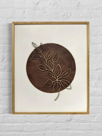 A product shot of the framed leaf art against a white brick wall, highlighting its clean and simple aesthetic.