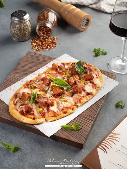 This flatbread pizza is styled with a glass of wine and spice shakers to create a sophisticated, Italian restaurant vibe. The composition guides the eye from the menu to the dish itself.