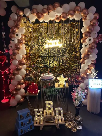 A full view of our gold and white birthday decor package. This setup includes a balloon arch, a shimmer curtain, a neon sign, and light-up 'HBD' letters.