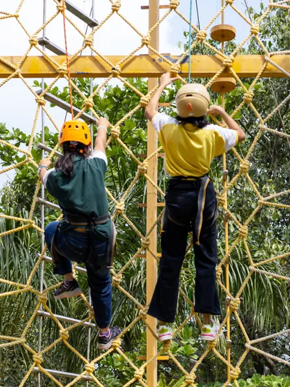 Two young climbers ascend the rope net, showcasing their determination. We ensure all our adventure activities are equipped with the highest safety standards.