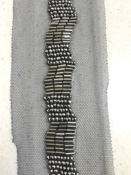 A detailed shot of a wavy, geometric beaded lace. The pattern is formed by arranging metallic bugle beads on a sheer net fabric, perfect for adding texture and shine to necklines or cuffs.