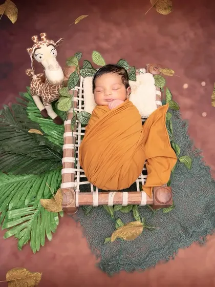 A wider view of the jungle-themed setup, with a baby sleeping soundly on a miniature charpoy. The falling leaves and rich, warm backdrop create a dynamic and enchanting scene.