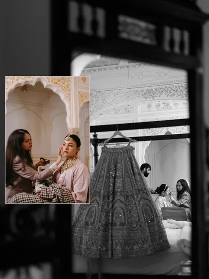 A creative black and white shot showing the bride getting her makeup done, reflected in a mirror where her wedding lehenga hangs in the foreground.