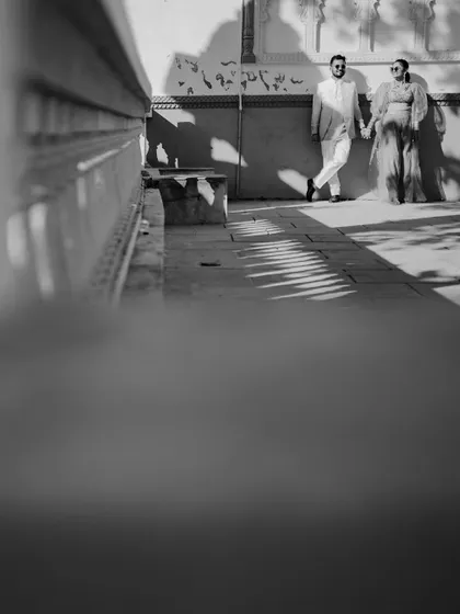 An artistic black and white shot using a low angle and foreground blur. This creative composition creates a sense of scale and drama, focusing on the couple against the wall.