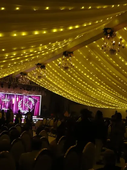 A grand stage setup for a 50th Golden Anniversary celebration. The large LED screen displays the couple's photo, and the ceiling is draped with fabric and fairy lights, creating a golden, celebratory glow.