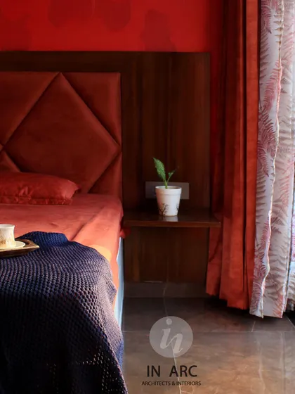 A close-up of a bedroom with a rich, warm color palette. The diamond-tufted headboard in deep red and the wooden side table create a cozy and inviting atmosphere.