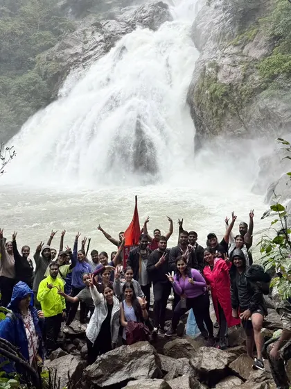 Our group celebrating with hands in the air in front of the mighty Dudhsagar falls. The energy and excitement are contagious.