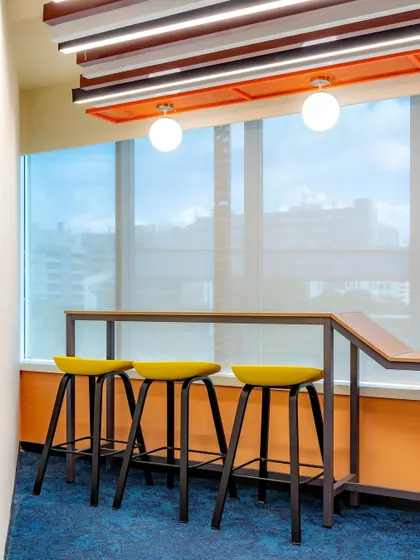This wider shot shows the yellow bar stools at a high-top counter overlooking a window, creating a perfect spot for employees to enjoy a coffee with a view.
