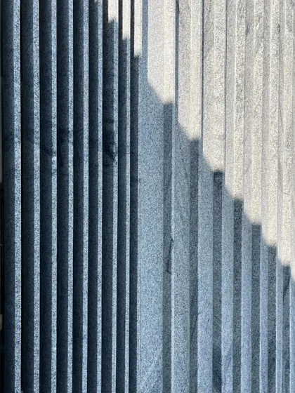 The play of light and shadow on a fluted stone facade. We love exploring how different material textures interact with sunlight throughout the day. This is a detail from a residential project under construction.