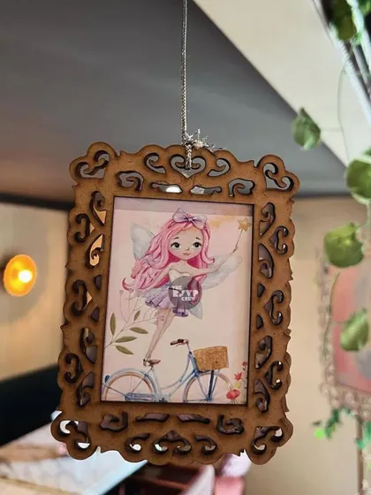 A close-up of one of the hanging wooden frames, featuring a sweet illustration of a pink-haired fairy on a bicycle.