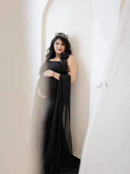 A powerful and mysterious portrait. The mom-to-be, wearing a crown and a black gown, is partially obscured by white curtains, creating an artistic and intriguing image.