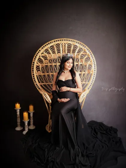 A "queen mama" portrait. Seated on a wicker peacock throne, this mom-to-be exudes confidence and style in a black gown and tiara.