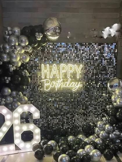 A glamorous 26th birthday setup with a black and silver sequin wall. The decoration features a "Happy Birthday" neon sign, marquee numbers, and a matching balloon arrangement.