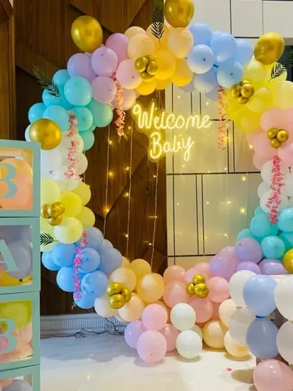 A pastel-colored 'Welcome Baby' setup with a circular balloon arch, neon sign, and 'BABY' boxes.