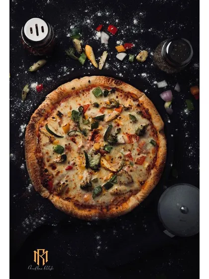 A full view of a vegetable pizza, styled with scattered ingredients on a dark surface. This shot provides a clear, top-down look at the product, suitable for menus and promotional flyers.