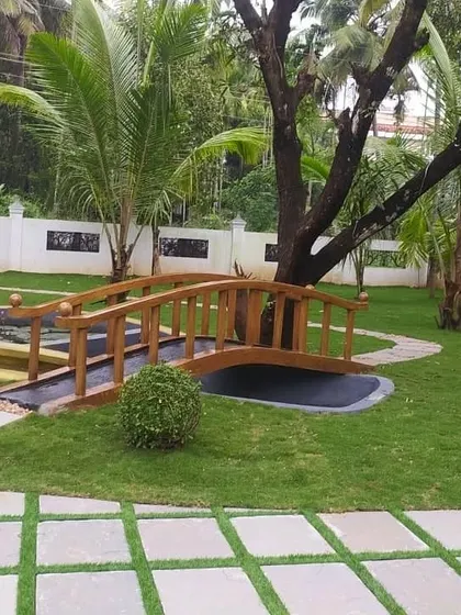 A charming wooden bridge over a dry creek bed or pond feature adds a whimsical touch to this garden. This element connects different parts of the lawn while serving as a beautiful focal point in the landscape design.