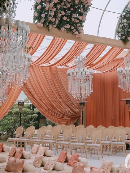 The ceremony seating was a mix of classic chairs and floor seating with custom-printed cushions. The space is defined by peach-colored drapes and magnificent crystal chandeliers.